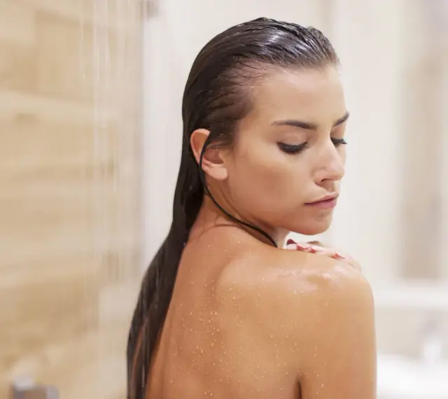 Mujer en la ducha, con gotas de agua en su piel. Pregúntate cada cuanto exfoliar el cuerpo para una piel radiante.